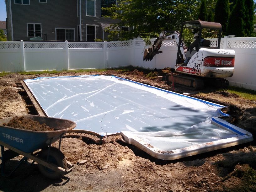 A bobcat is working on a swimming pool in a backyard