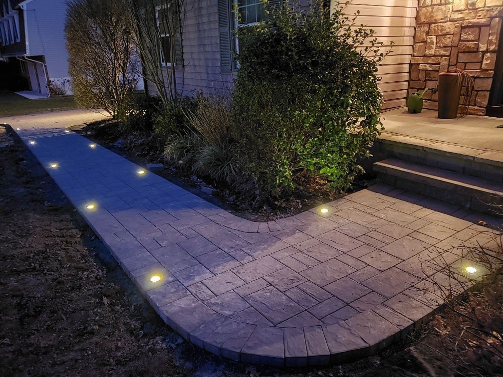 A brick walkway is lit up at night in front of a house