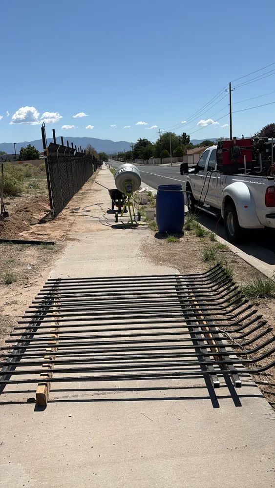 Concrete sidewalk blocked by bent metal rebar in a construction area beside parked trucks.