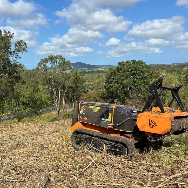 An Orange and Black Tractor is Parked in a Field With Trees — NQ Steep Terrain Mulching and Clearing in The Leap, QLD