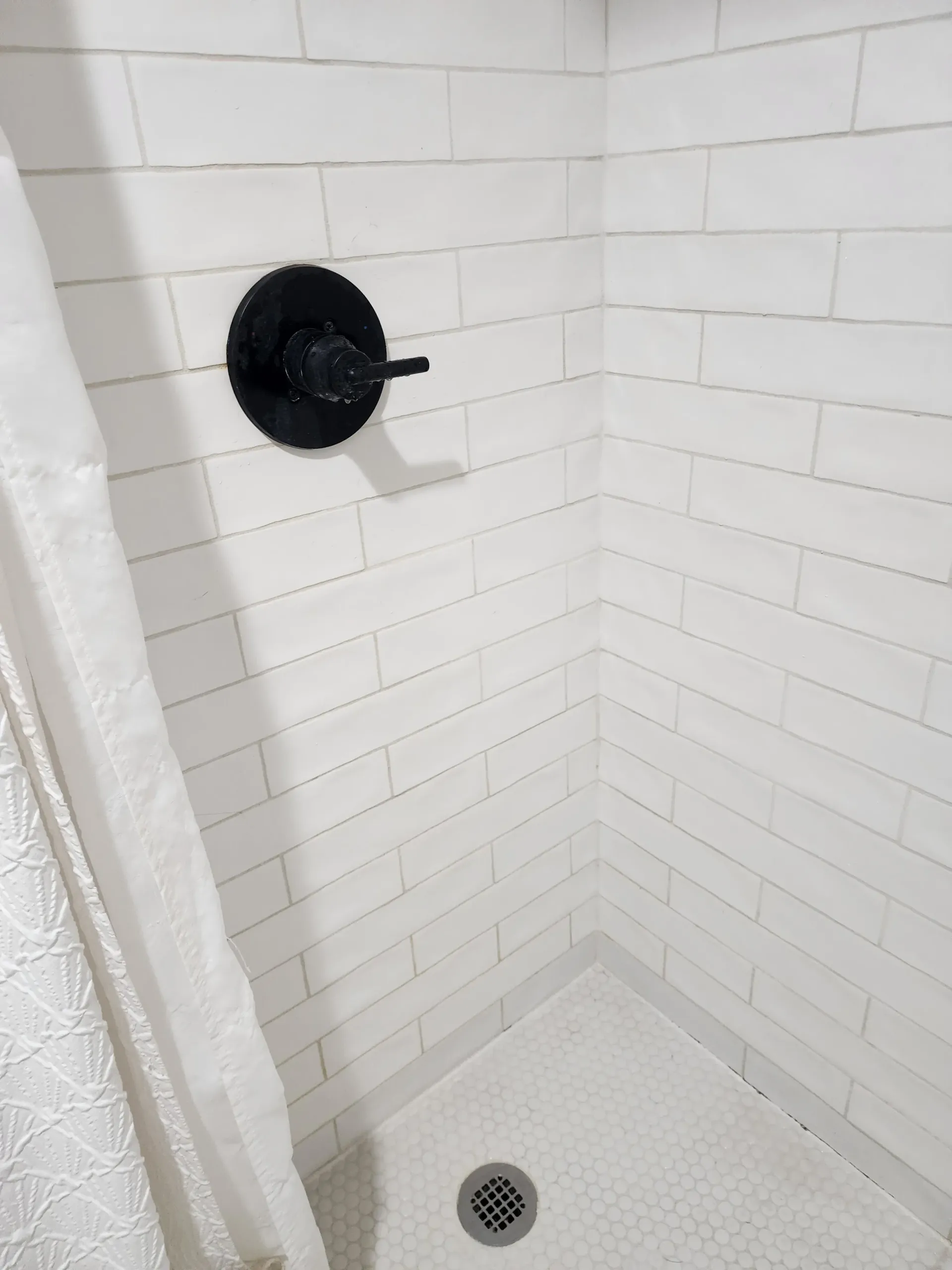 a shower stall with white tiles and a black shower head .