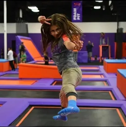 A girl is jumping on a trampoline in front of a banner that says foam fit