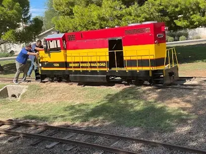 A red and yellow train is on the tracks in a park.