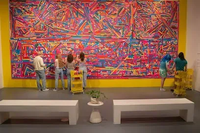 A group of people are standing in front of a large colorful painting on a wall.