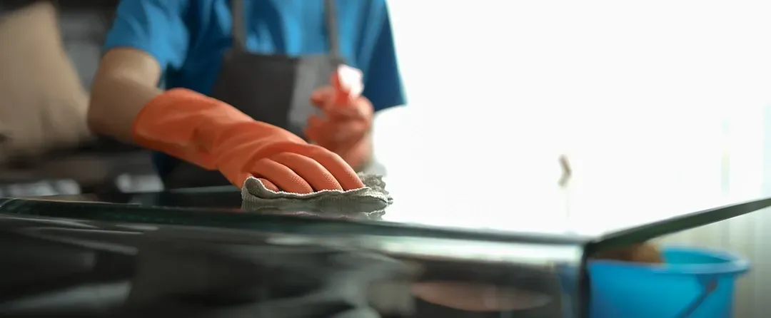 A person wearing orange gloves is cleaning a glass table with a sponge.