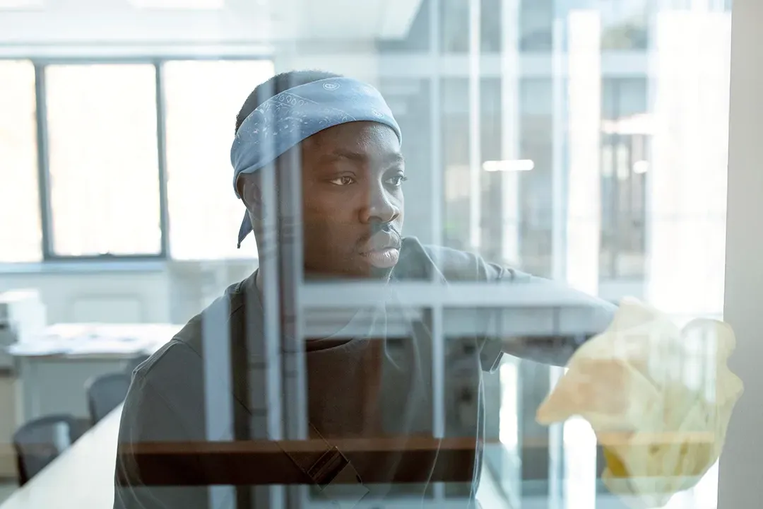 A man wearing a bandana is looking out of a window.