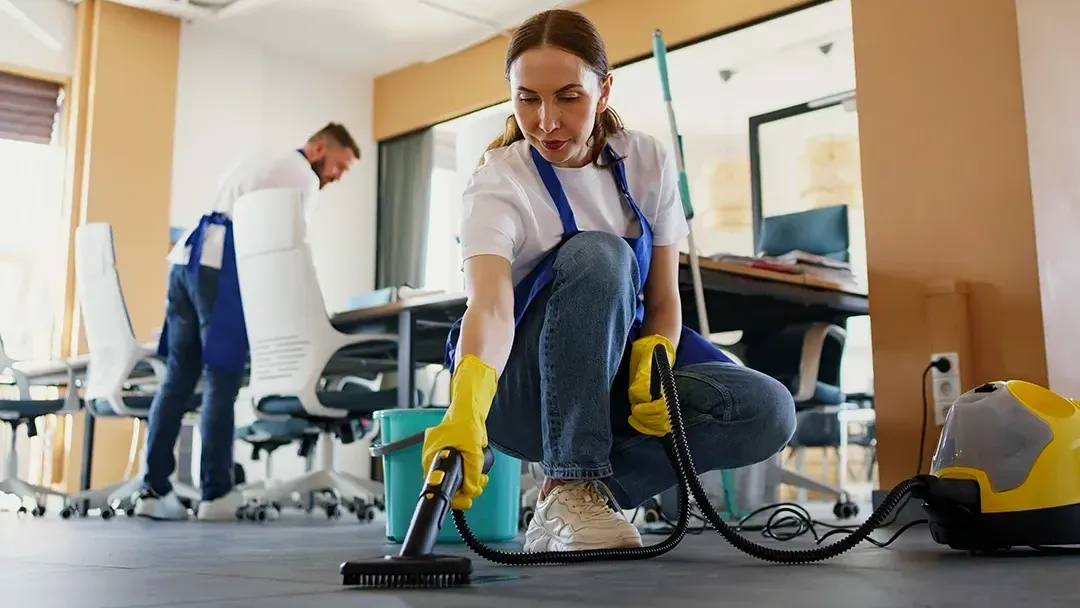 A woman is cleaning the floor of an office with a vacuum cleaner.