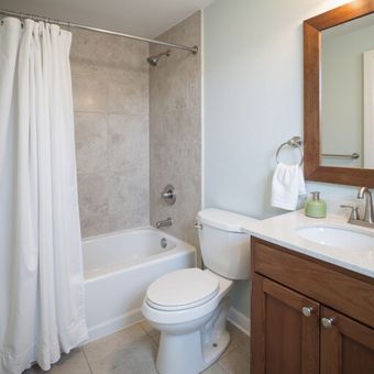 Bathroom with a bathtub, toilet, sink, and mirror. White curtain, light blue walls, and brown cabinet.
