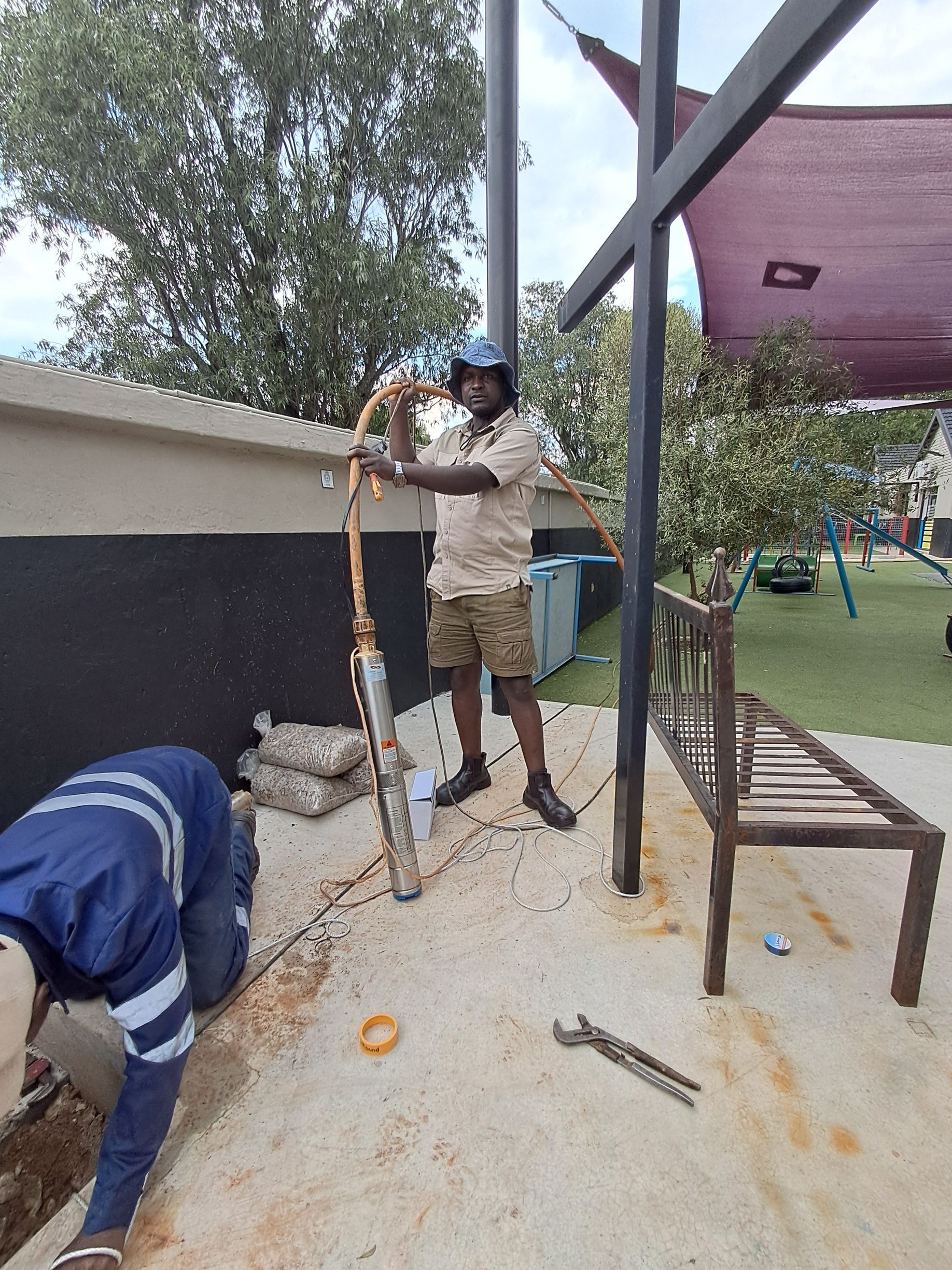 Two men are working on a borehole in a garden.