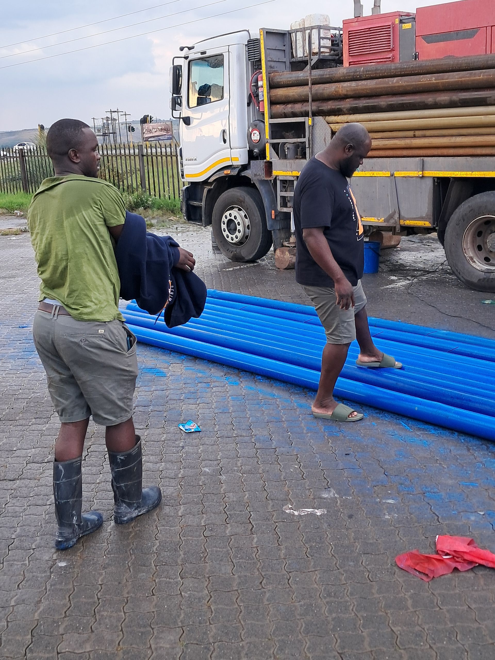 Two men are standing next to a truck carrying blue pipes.