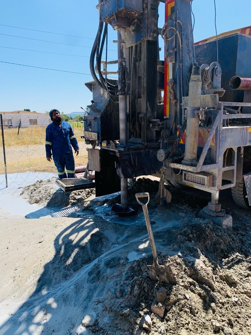 A man is standing next to a large machine in the dirt.