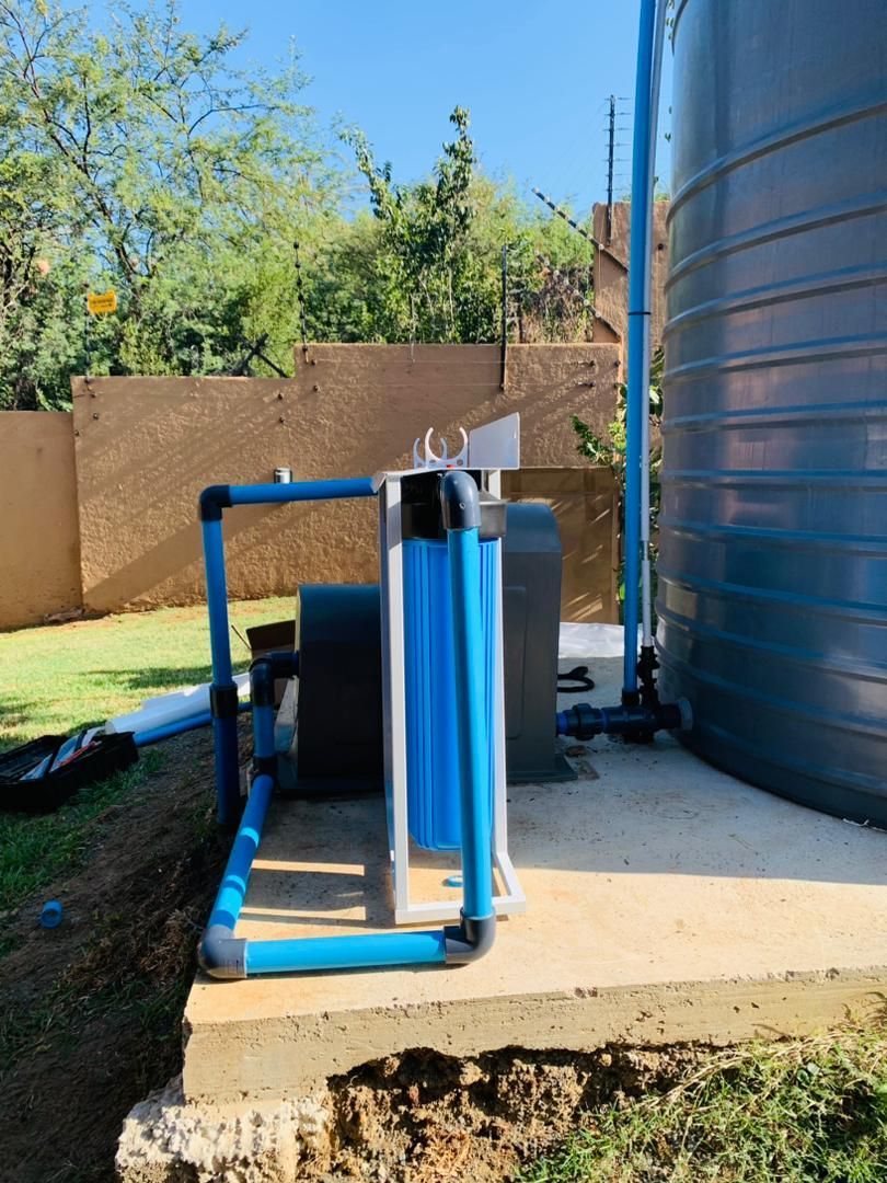 A blue pipe is connected to a water tank in a backyard.