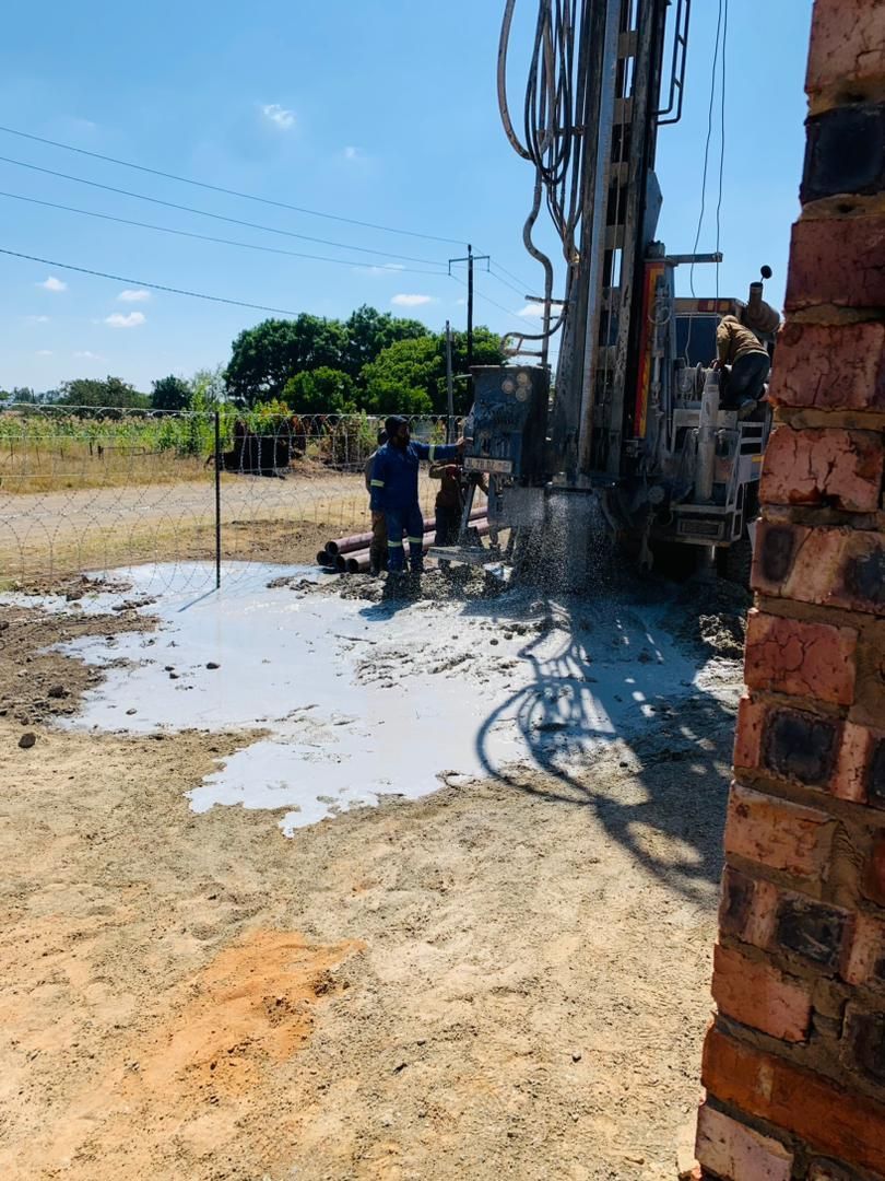 A man is standing next to a drill in a dirt field.