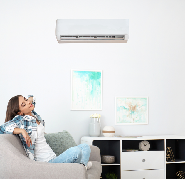 A woman is sitting on a couch in a living room under an air conditioner.