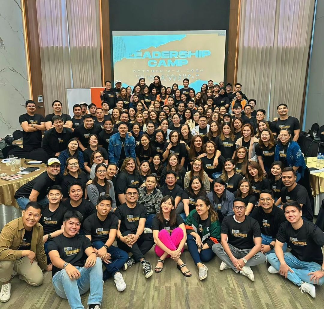 A large group of people are posing for a picture in front of a screen that says leadership camp
