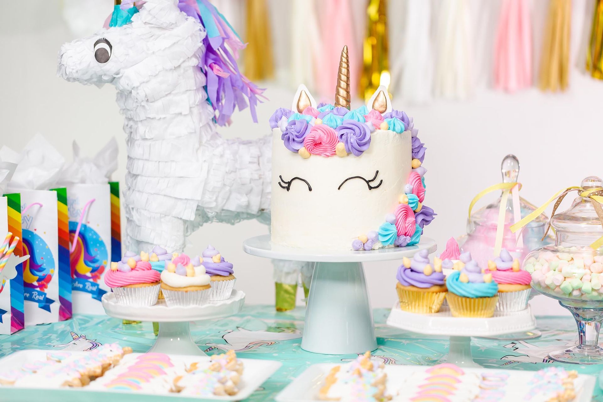 A table with a unicorn cake and cupcakes on it.