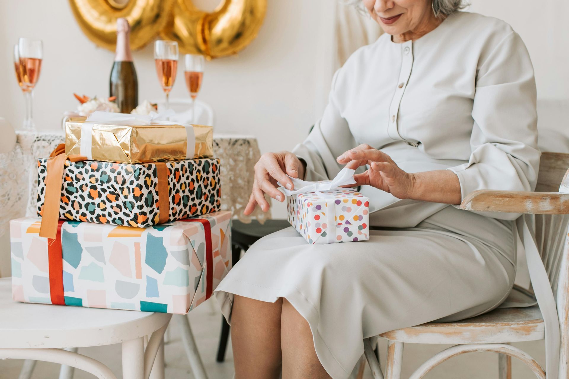 An elderly woman is sitting in a chair opening a gift box.