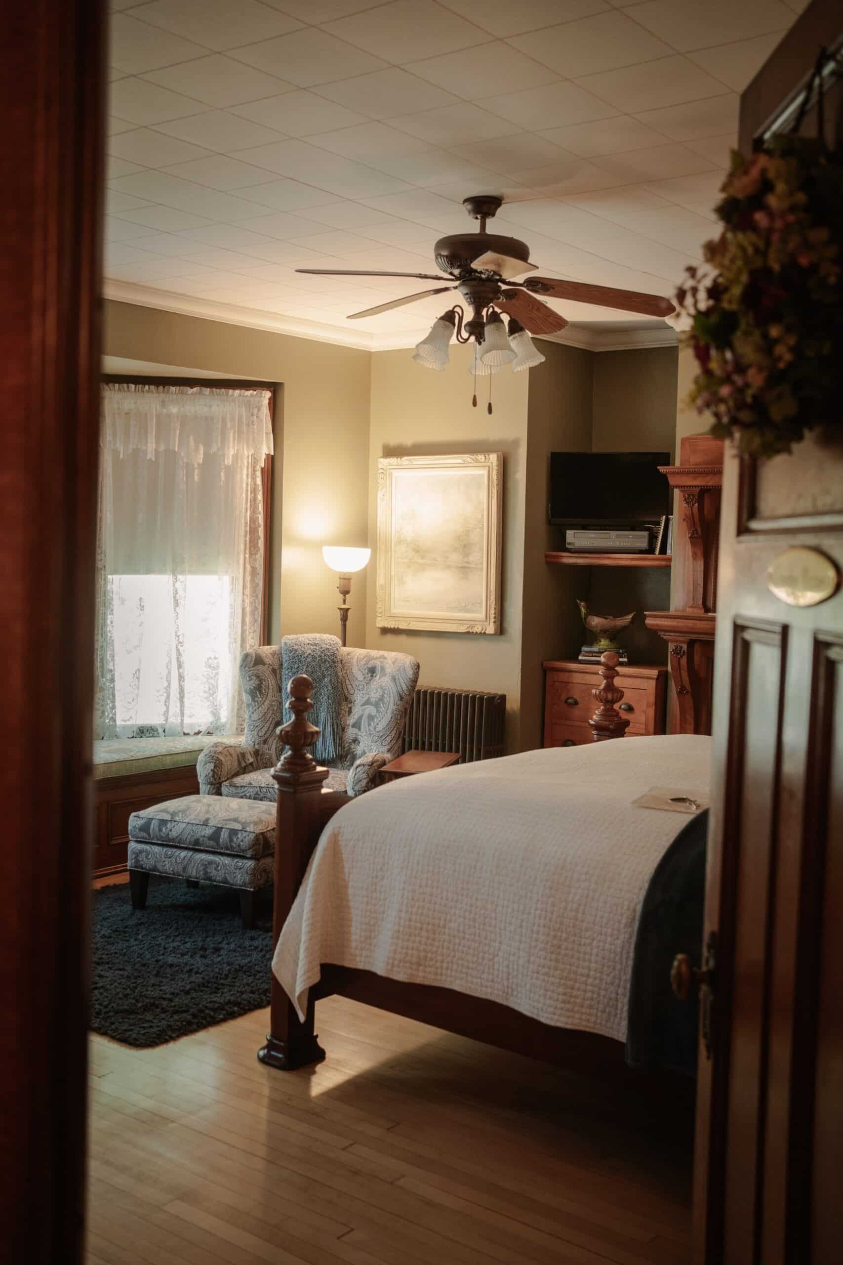 A bedroom with a bed , chair , lamp and ceiling fan.