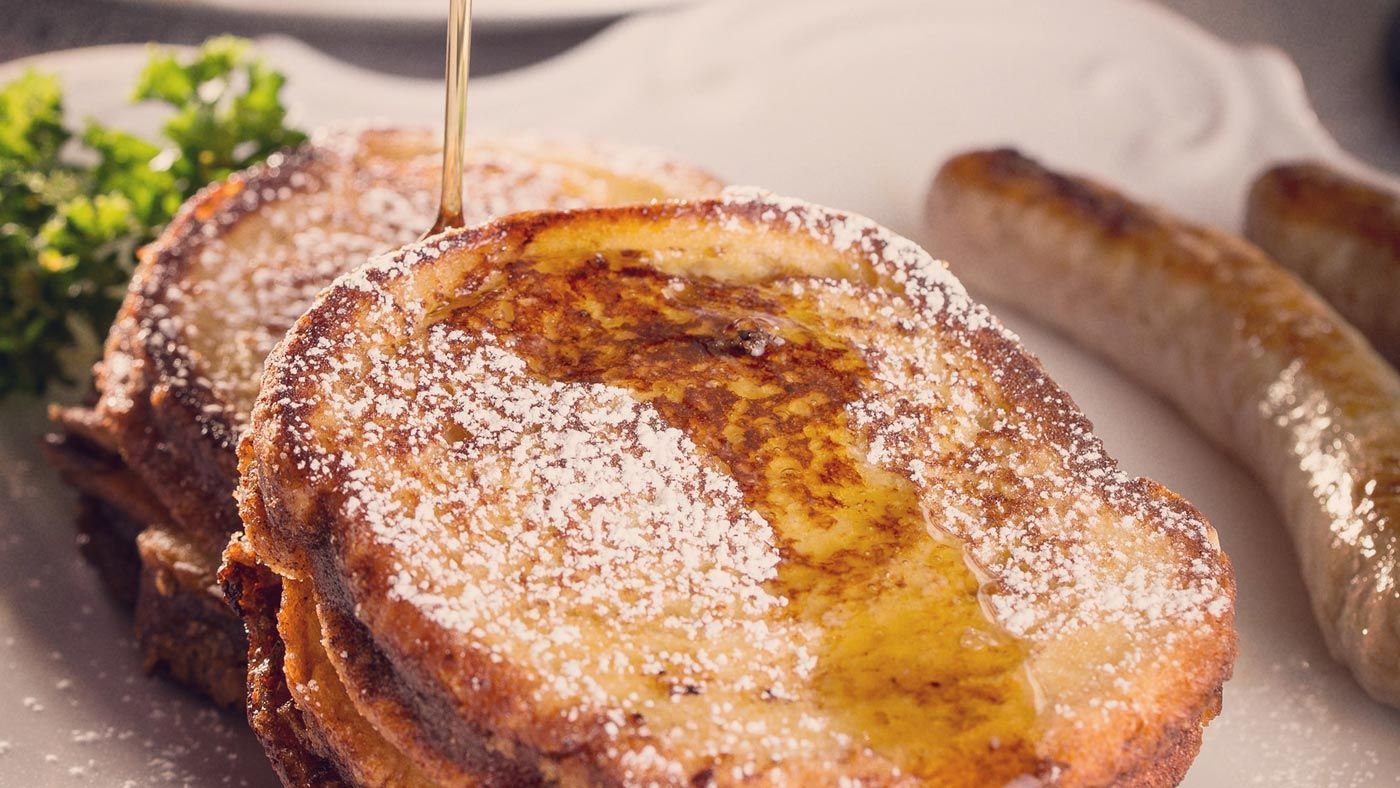 A plate of french toast with syrup and sausages on a table.