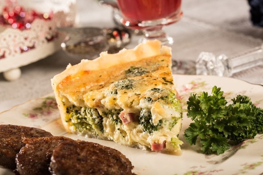 A slice of quiche is on a plate with meatballs and parsley.