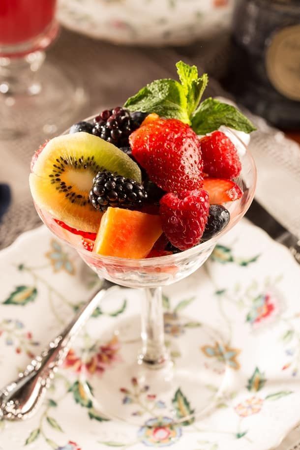 A martini glass filled with fruit and mint on a plate.