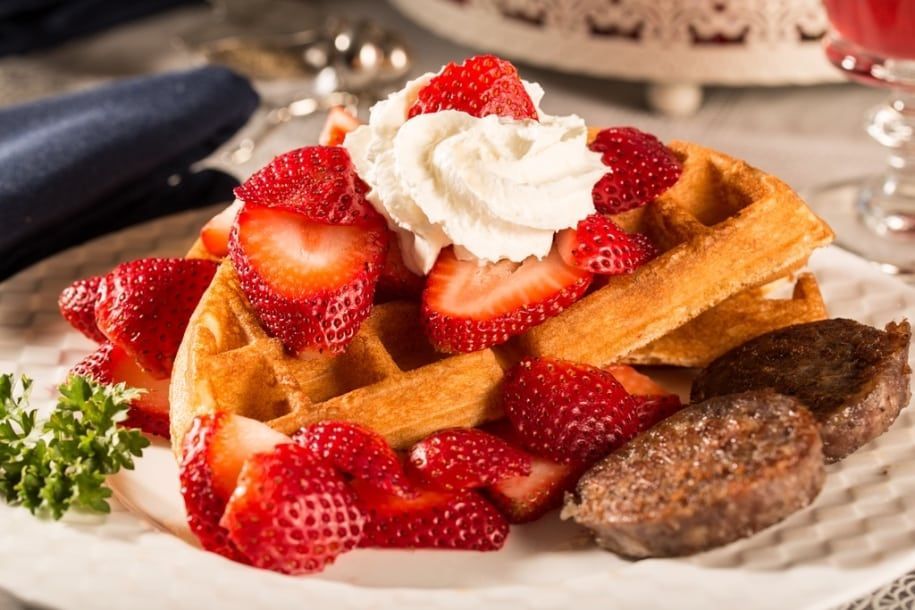 A white plate topped with waffles strawberries and whipped cream