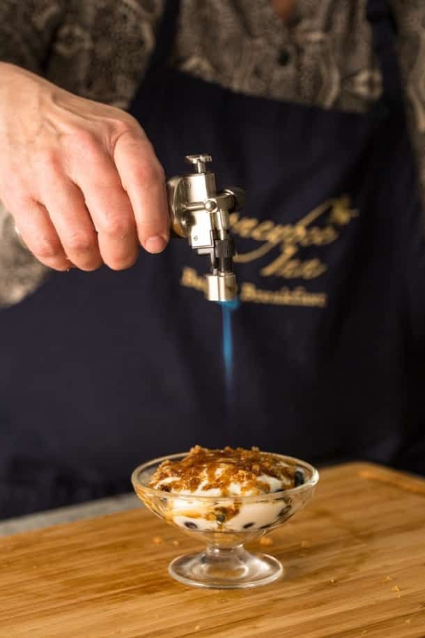 A person is lighting a dessert with a torch.