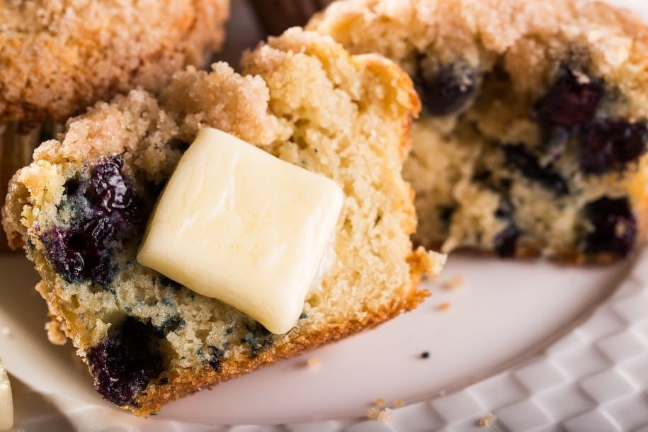A close up of a muffin with butter on it on a plate.