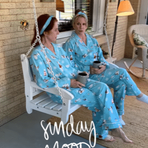 Two women in blue pajamas are sitting on a porch swing.