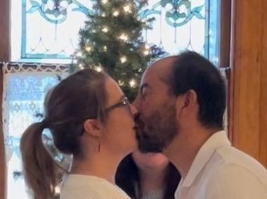 A man and a woman are kissing in front of a christmas tree.