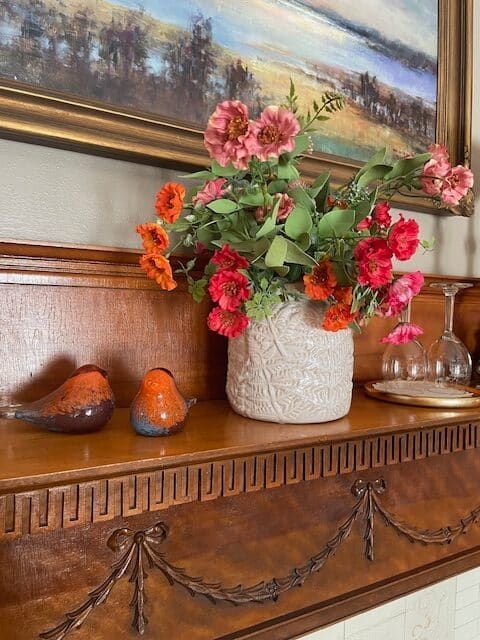 A vase of flowers is sitting on a wooden shelf next to a painting.