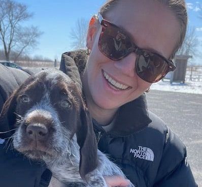 A woman wearing sunglasses is holding a brown and white dog.