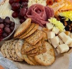 A tray of crackers , cheese , grapes , olives and meat on a table.