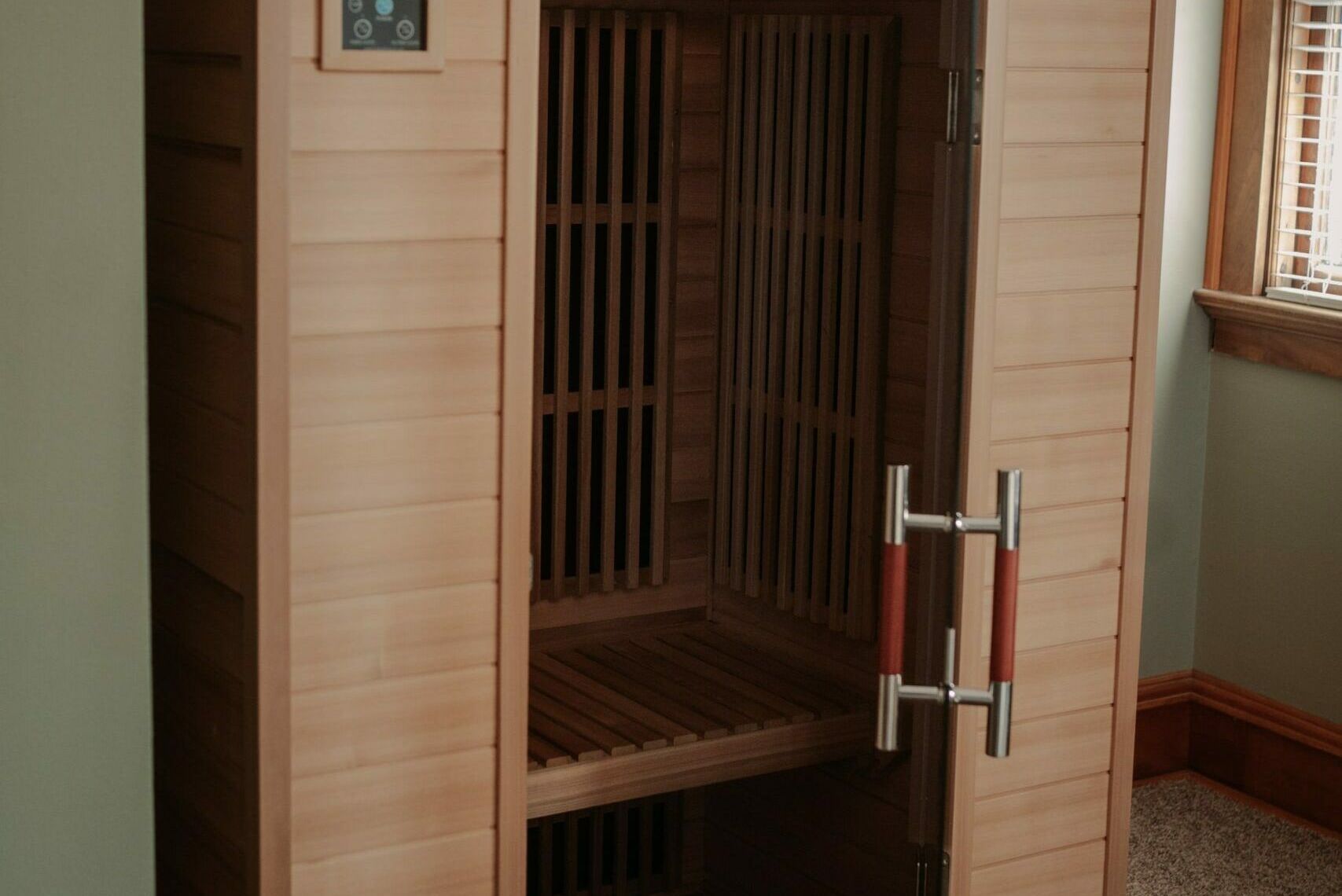 A wooden sauna is sitting in a room next to a window.
