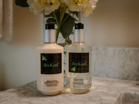 Two bottles of beekind lotion and hand soap are sitting on a bathroom counter next to a vase of flowers.