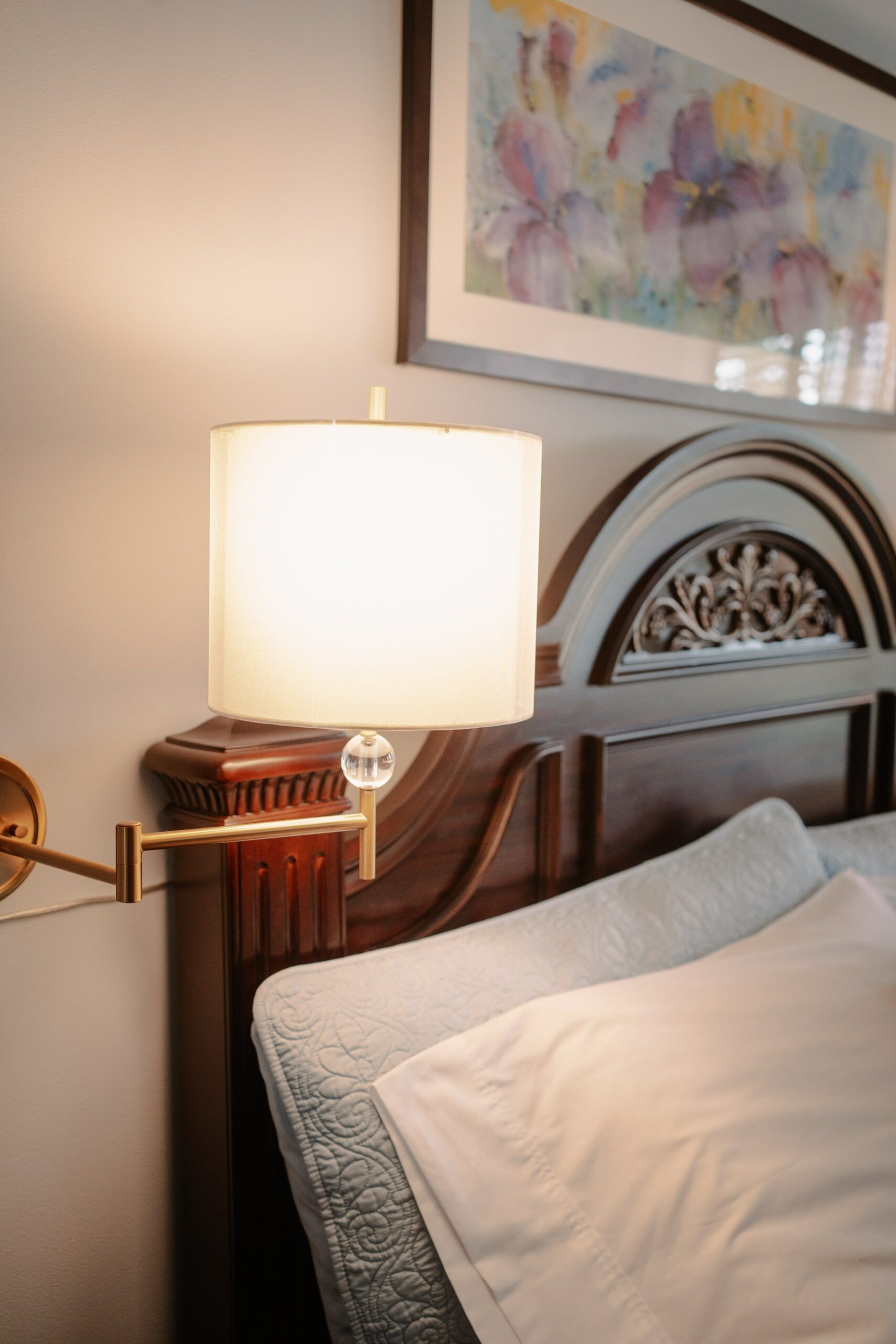 A bed with a lamp on the side of it and a picture on the wall above it.