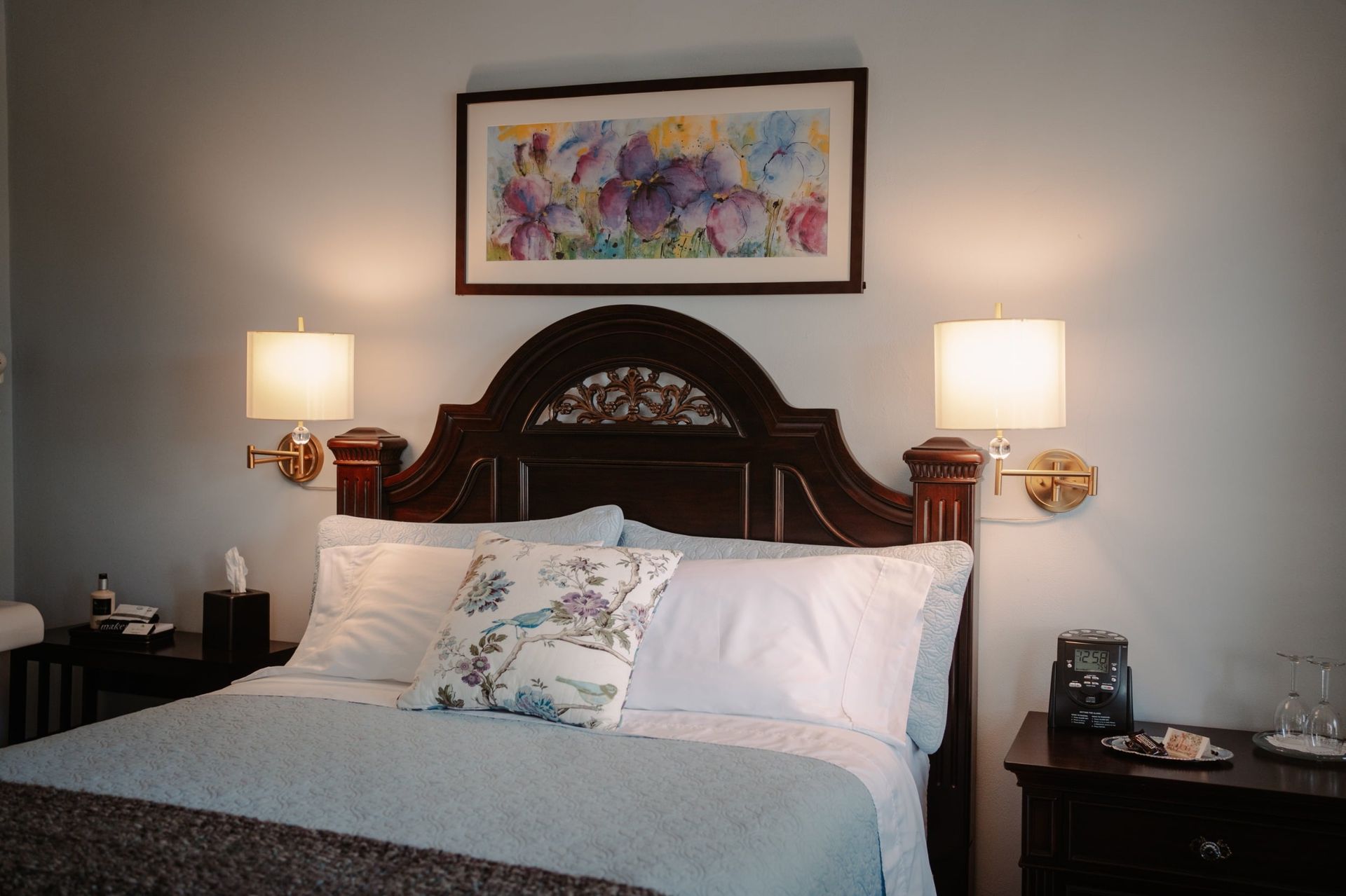 A bedroom with a bed , nightstand , lamps and a picture on the wall above the bed.