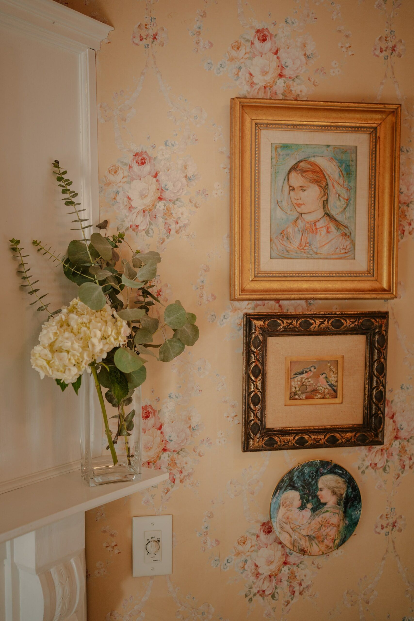 A vase of flowers is sitting on a shelf next to a painting on a wall.