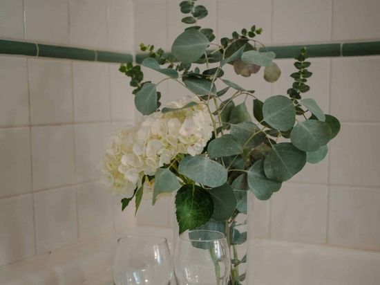 A vase filled with white flowers and green leaves is sitting on a bathtub.