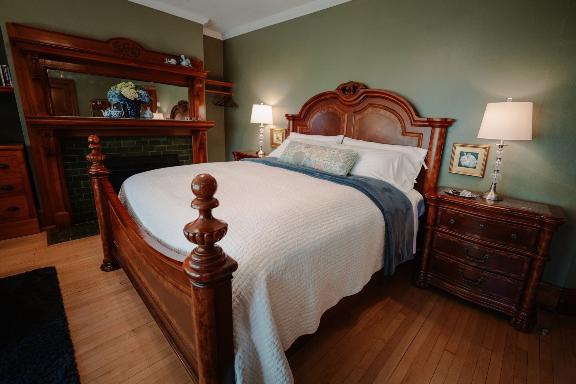 A bedroom with a bed , nightstand , dresser and fireplace.