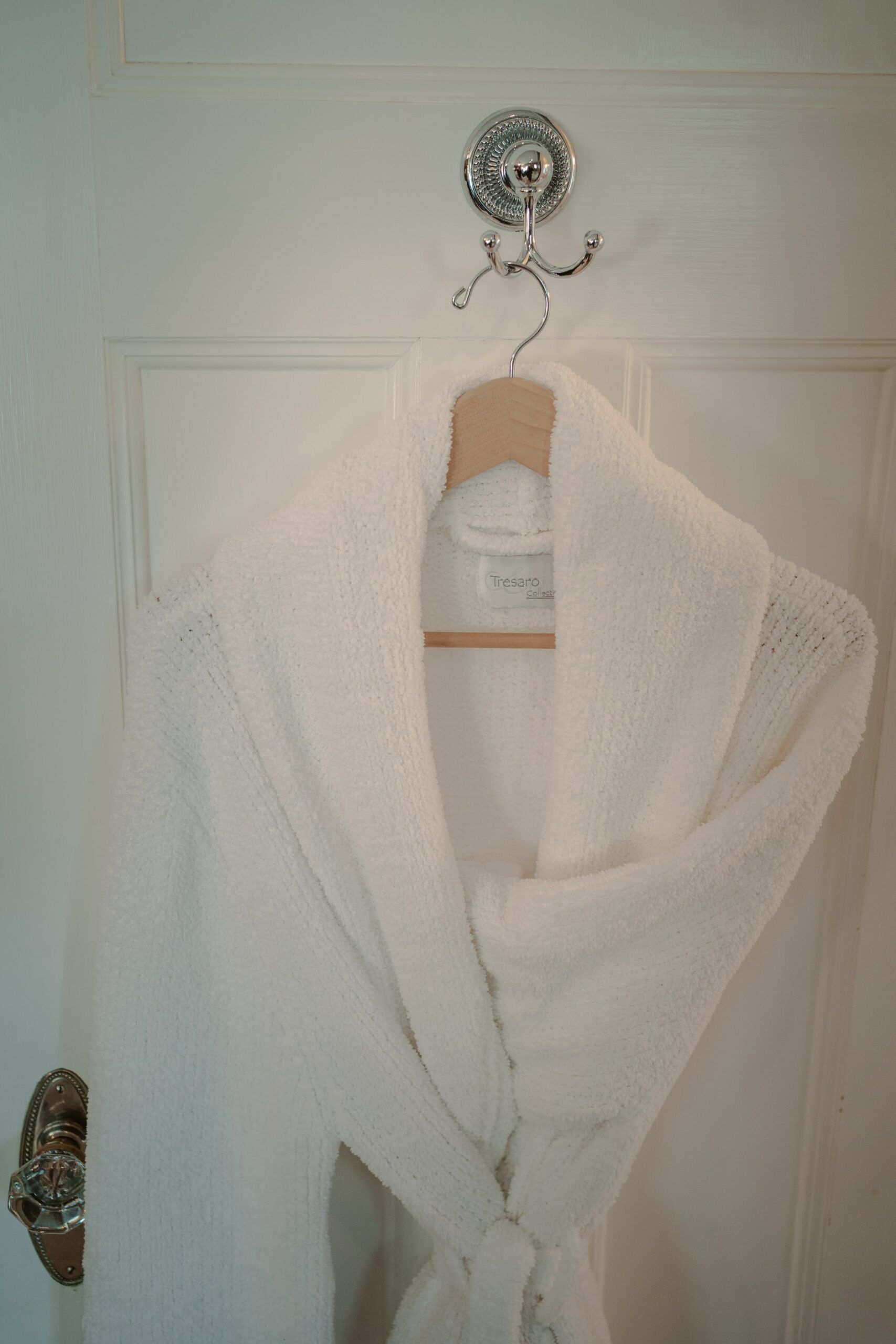 A white robe is hanging on a hook on a door.