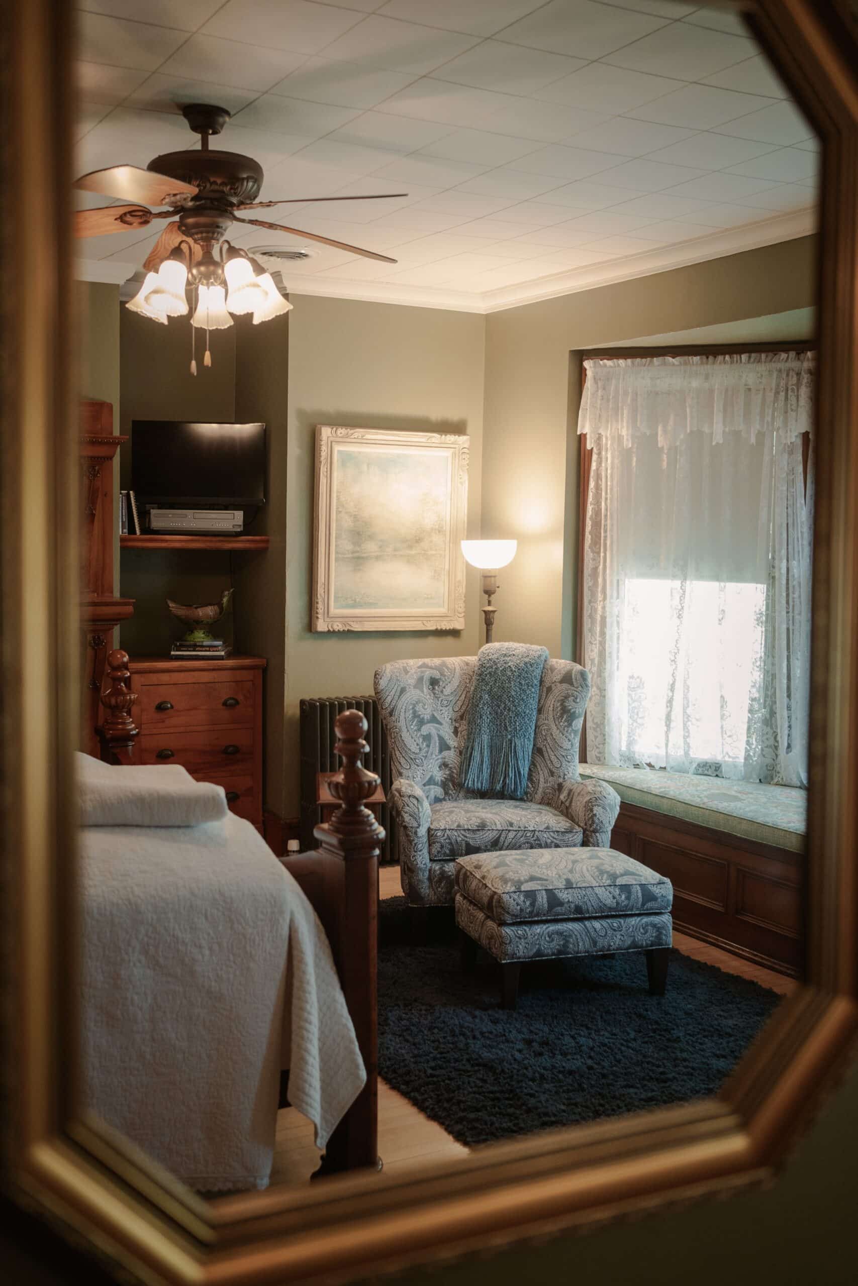 A bedroom with a chair and ottoman is reflected in a mirror.