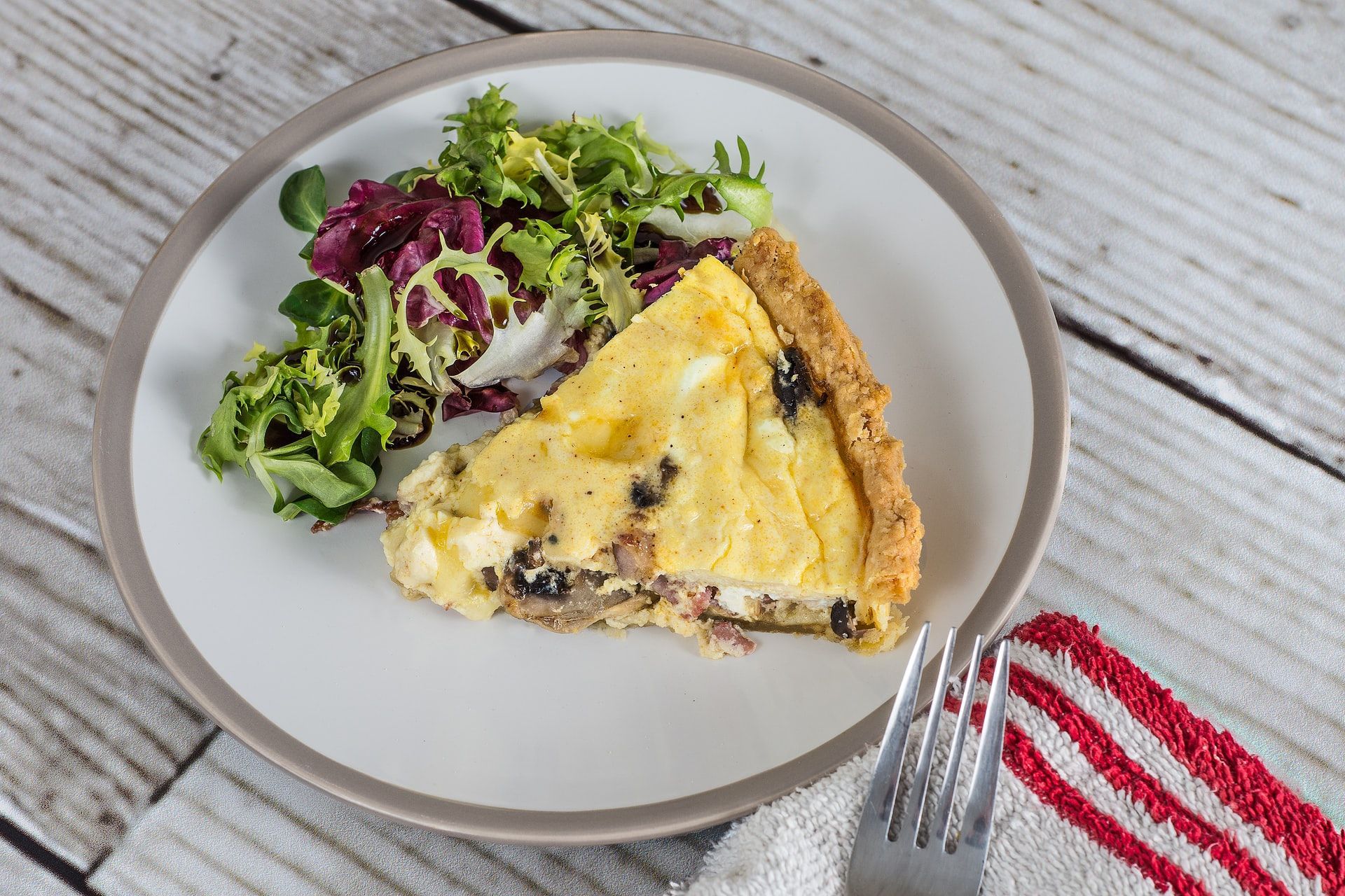 A slice of quiche and a salad on a plate with a fork.