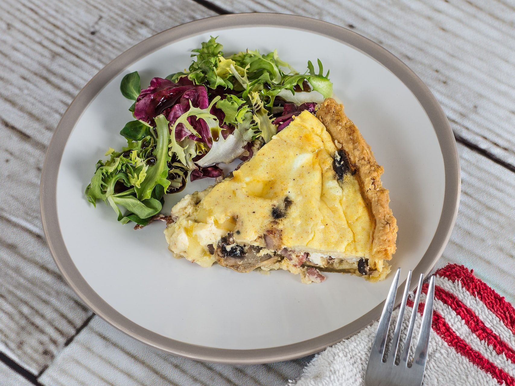 A slice of quiche and a salad on a plate with a fork.