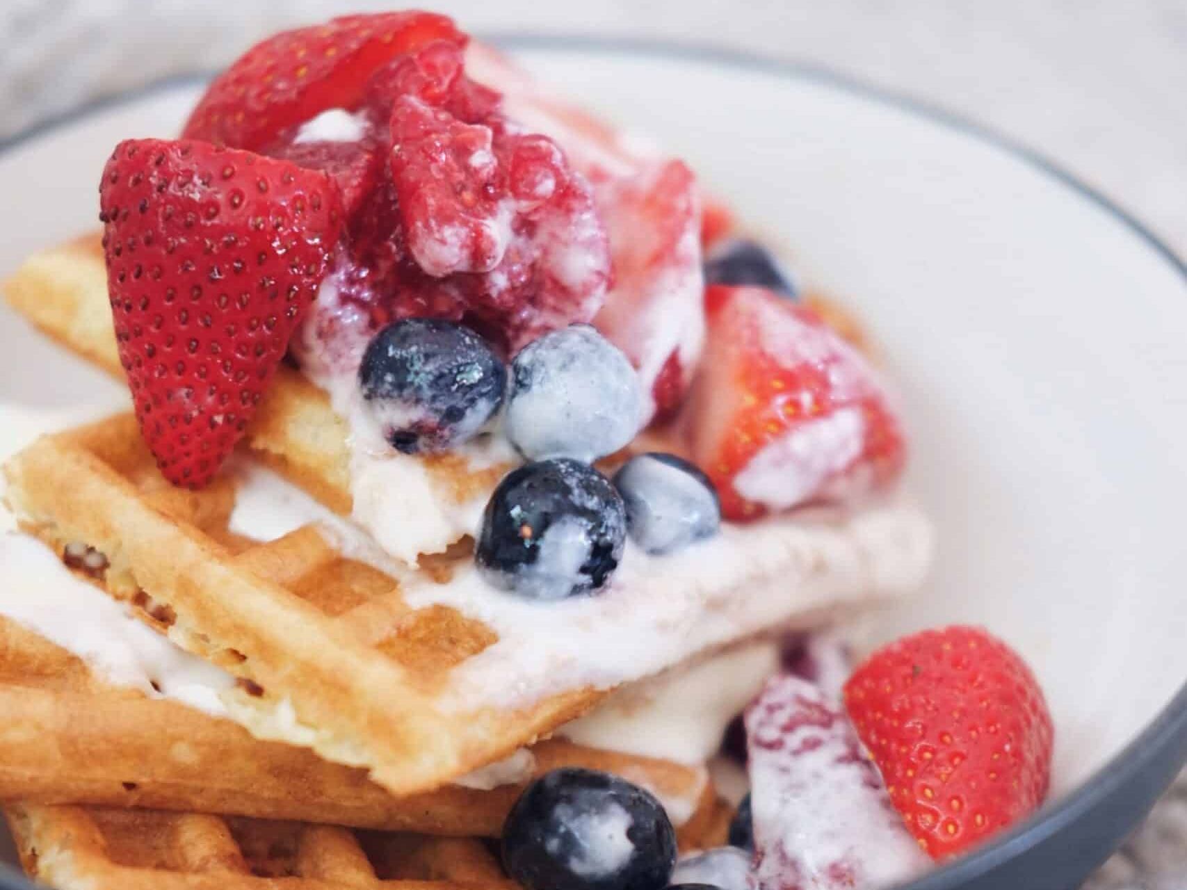 A bowl of waffles with strawberries and blueberries on top.