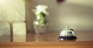 A hotel bell is sitting on a wooden table next to a vase of flowers.