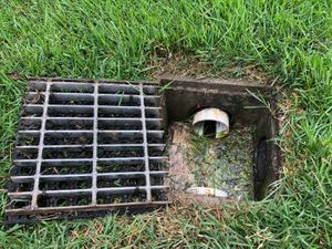 A manhole cover is sitting in the grass next to a drain.