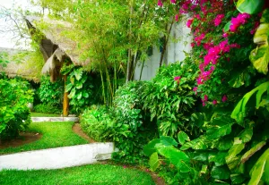A lush green garden with pink flowers and a thatched roof