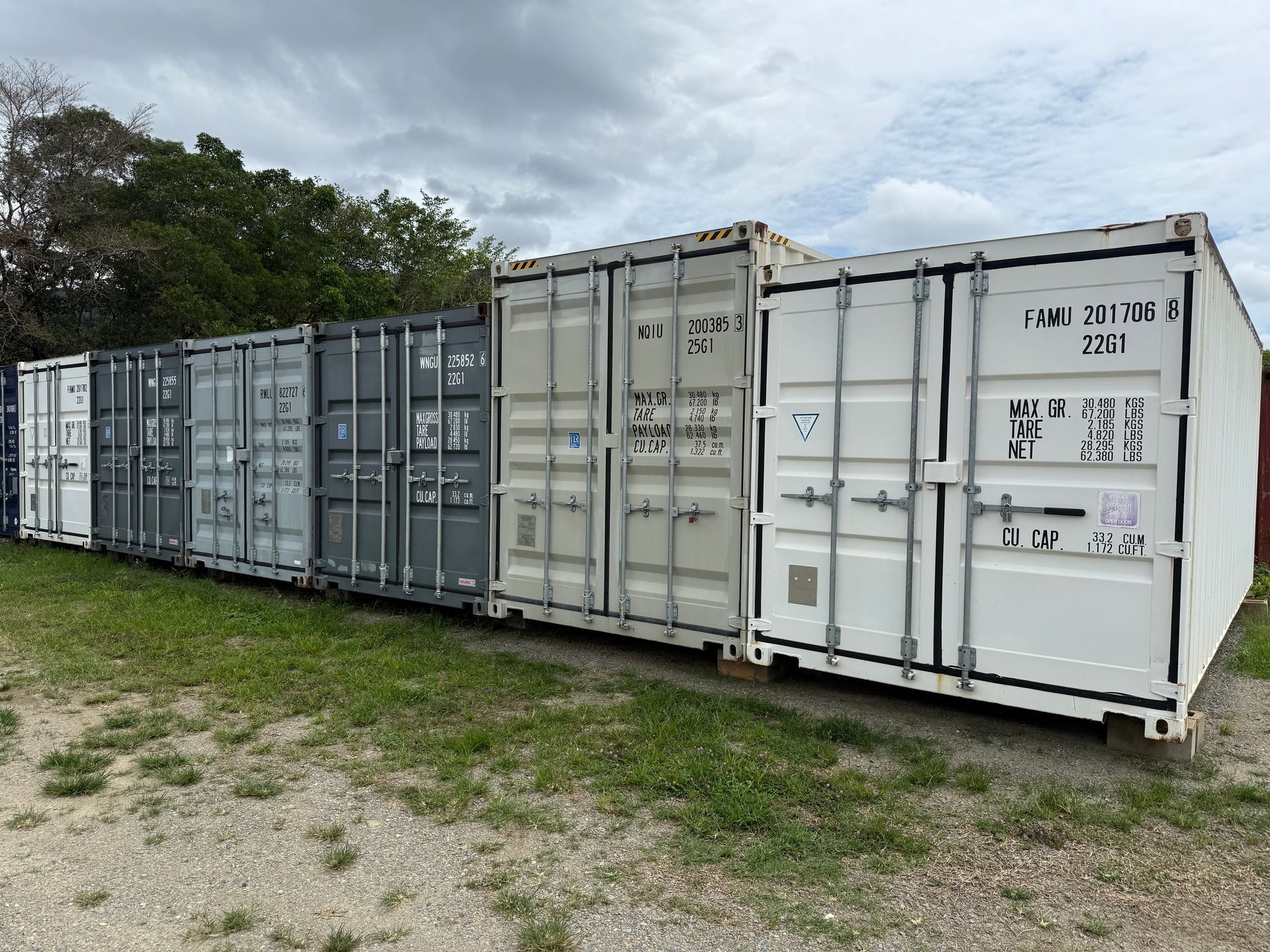 Shipping containers, various colors, lined up outdoors on a grassy area — Cairns Budget Storage In Mount Sheridan, QLD
