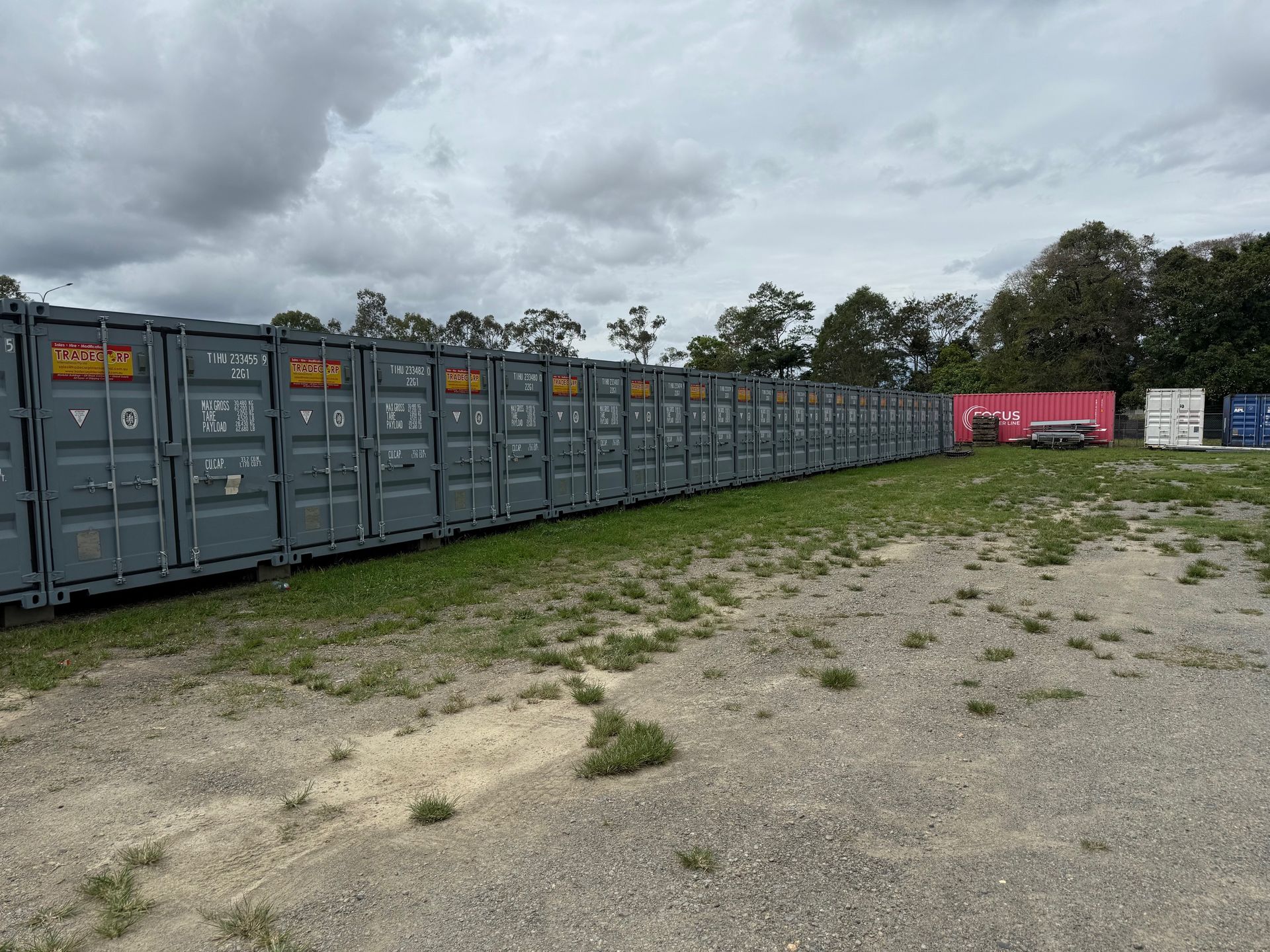 Row of grey shipping containers on a gravel lot, under a cloudy sky.— Cairns Budget Storage In Mount Sheridan, QLD